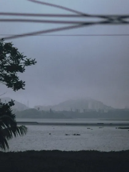 A moody, atmospheric shot of Powai lake during the monsoon. The distant hills and buildings are shrouded in fog, creating a sense of calm and mystery.