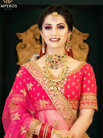 Add a vibrant pop of color to your wedding ensemble. This stunning gold-plated bridal set features a mix of colorful stones in a navratan style, paired with a bright pink lehenga for a joyful and unforgettable look.