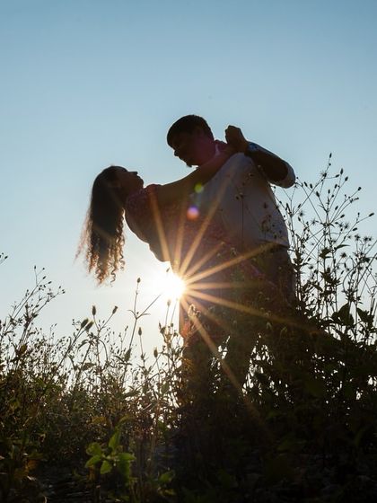 A romantic silhouette of a couple dancing in a field at sunset. The sunburst effect and the natural setting make this a dreamy and magical shot.