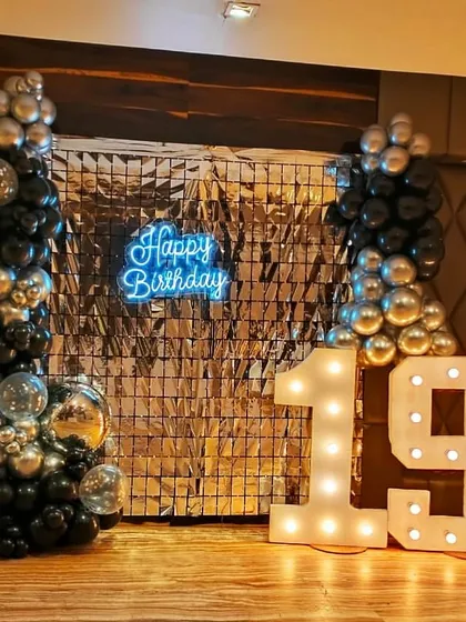 Celebrating a 19th birthday with a cool, modern aesthetic. This party decor features a silver shimmer wall, a custom blue 'Happy Birthday' neon sign, marquee LED numbers, and stylish black and silver balloon columns.