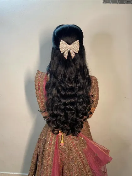 For a glamorous reception, I styled this client's hair in voluminous, bouncy curls. The look is completed with a modern, sparkling bow clip, creating a half-updo that is perfect for dancing the night away.