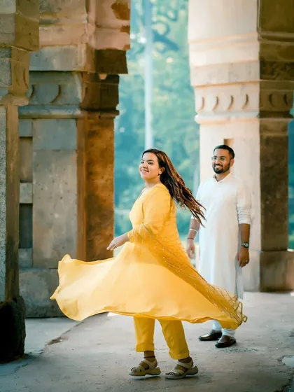 A dynamic shot of the bride twirling in her yellow suit, creating a sense of movement and joy. The historical architecture of Lodhi Garden provides a beautiful backdrop.