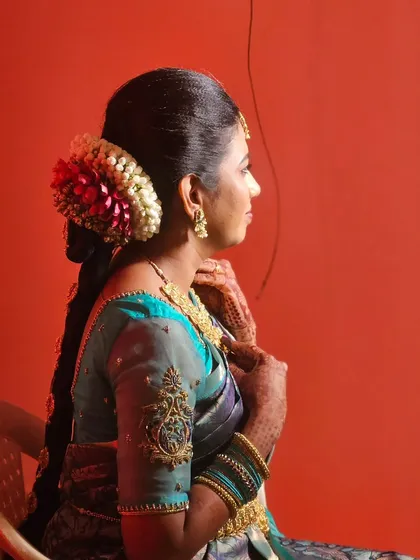 A side view of a traditional bridal hairstyle, showing the neat bun adorned with jasmine and red flowers, leading into a long, decorated braid.