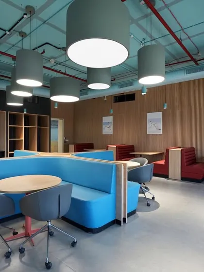 A breakout area with diner-style booth seating in bright blue and red. The large drum pendant lights provide soft, diffused lighting.