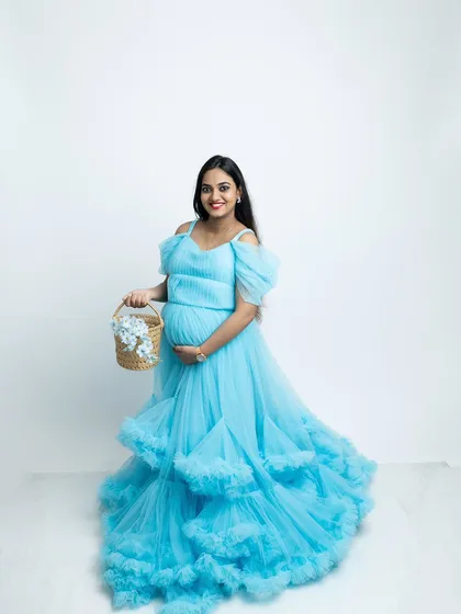 Adding a simple prop like a basket of flowers can bring a touch of softness and detail to a maternity portrait. The mother-to-be looks radiant in her blue gown against the simple white backdrop.
