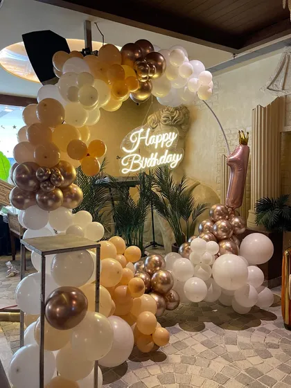 A chic and elegant first birthday setup with a neutral color palette. The white and gold balloon arch, "Happy Birthday" neon sign, and a number '1' foil balloon create a sophisticated look.