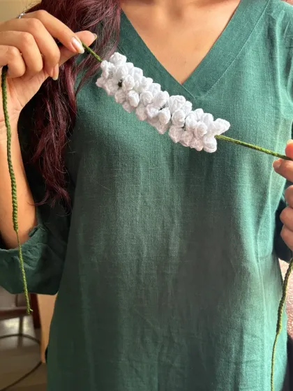 This photo shows the full length of the crochet gajra with its green tie-strings. It's long enough to be styled in many different ways, whether in a bun or a braid.