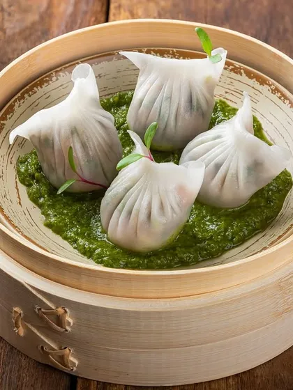 Delicate steamed dumplings on a bed of green chutney, presented in a bamboo steamer. This image highlights a creative and modern take on serving dim sum.