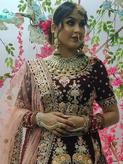 This bride is wearing a deep maroon velvet lehenga with silver floral embroidery, paired with a stunning emerald green jewellery set for a beautiful contrast.