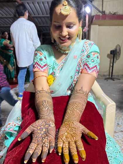 A happy bride displaying her freshly applied mehendi, with beautiful floral mandalas on the palms.