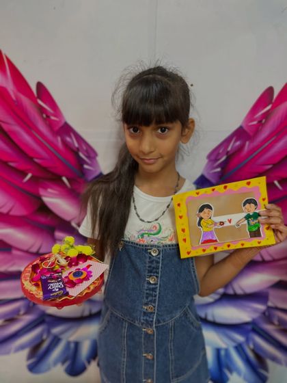 A student poses with her completed Rakhi gift set, including a handmade card and a decorated thali.