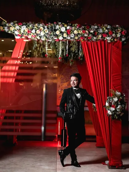 A stylish portrait of the groom at his engagement party. He leans against a doorway framed by red curtains, creating a cool and confident look that is both modern and classic.