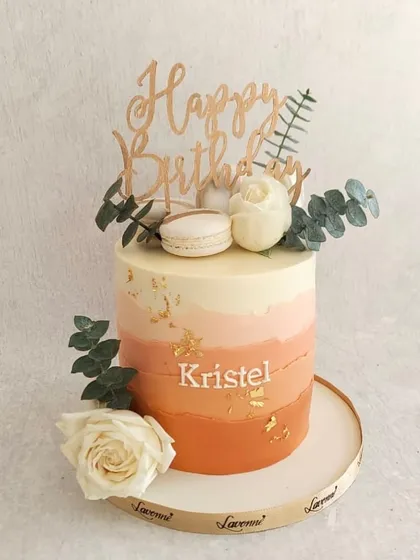 A beautiful cake in Peach Fuzz, the colour of the year. The soft ombre buttercream is decorated with fresh flowers, macarons, and a touch of gold leaf.