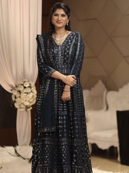 A full-length portrait of a client dressed for a reception. Her makeup is kept classic and elegant to complement her intricately designed navy blue Anarkali.