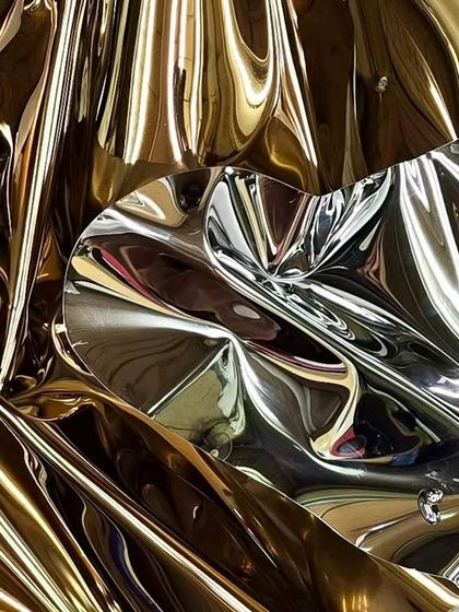 A close-up of "Meteor 142," revealing the intricate folds in the gold-toned stainless steel that create a complex play of light and shadow.