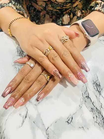 A glamorous set featuring long coffin-shaped nails with a mix of rose gold chrome, pink glitter, and rhinestone accents.