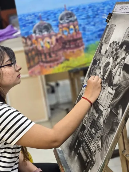 This image shows the student meticulously working on the figures in her large-scale charcoal drawing, demonstrating her focus and attention to detail.