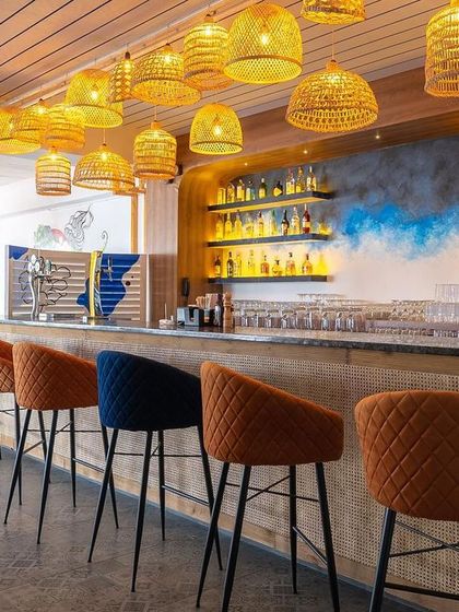 A different angle of the bar, showing the mix of orange and blue stools that add a pop of color. The back-lit shelves and hand-painted blue accent on the wall create depth and visual interest.