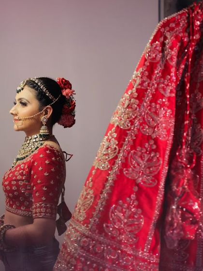 The bride, now fully ready, stands next to her lehenga. The color photo shows the vibrancy of her complete look.