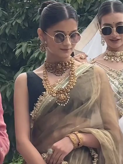 A modern take on traditional style. This model pairs a simple black blouse and an elegant organza saree with a heavy, antique gold temple jewellery set for a chic, contemporary look.