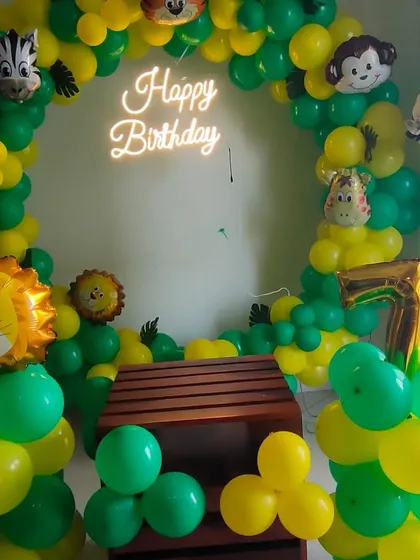 A compact jungle theme decoration for a home party, featuring a circular balloon arch with animal-head foil balloons and a neon sign.
