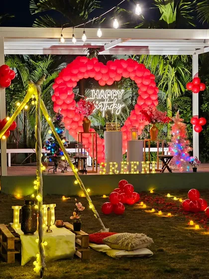 A wider view of the teepee and balloon heart combination setup at night. The entire lawn is illuminated with string lights and candles, creating a magical and celebratory environment.