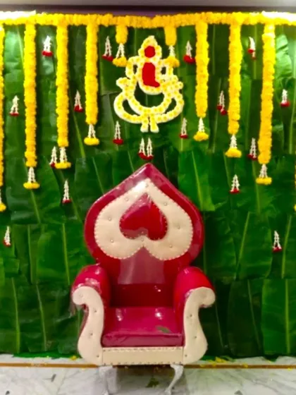 A traditional backdrop for a Half Saree ceremony using a wall of banana leaves. The decor is accented with marigold garlands and a central Ganesha motif made of flowers.