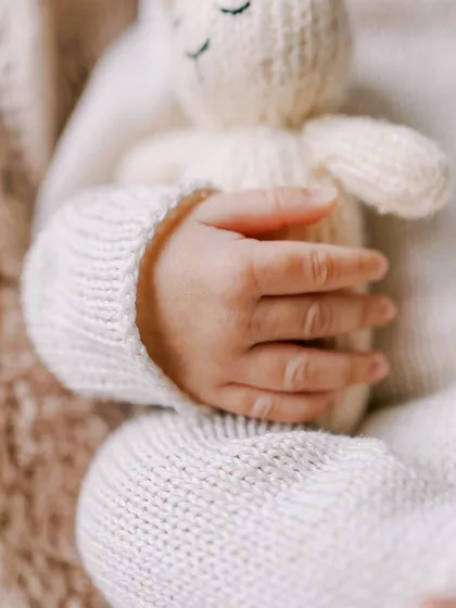 A close-up detail of a newborn's hand holding a tiny knitted bear, highlighting the delicate features and textures of the session.