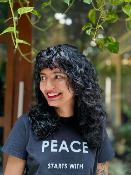 Curly bangs are the cutest! This client is radiating joy with her new fringe and layered cut that perfectly frames her smiling face.