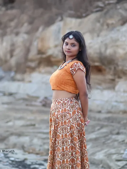 A bohemian-inspired ethnic look, featuring a printed skirt and crop top with silver jewelry. The rocky, outdoor setting complements the earthy tones of the outfit.