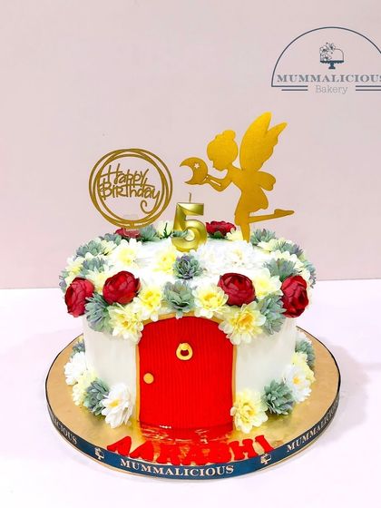 A cake straight out of a fairy house. This whimsical design with a little red door and a garden of buttercream flowers is perfect for a magical 5th birthday.