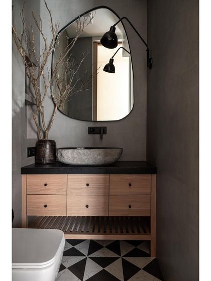 This chic powder bathroom features a black leather-finish marble basin counter that harmonizes with patterned flooring and fabric-finished wall tiles. A generously sized mirror enhances both elegance and the sense of spaciousness.