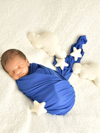 A sweet sleeping baby wrapped in blue, dreaming among soft, plushy stars and clouds. This simple themed setup adds a touch of whimsy to a classic newborn portrait.