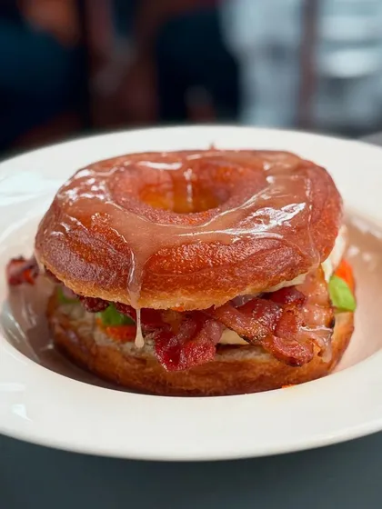 An indulgent, glazed breakfast doughnut sandwich from the Praça Prazeres pop-up, layered with crispy bacon and other delicious fillings.