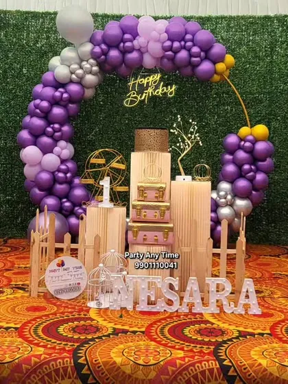 A full view of Nesara's first birthday decoration with a purple and silver color scheme. The setup includes a picket fence and vintage-style props.