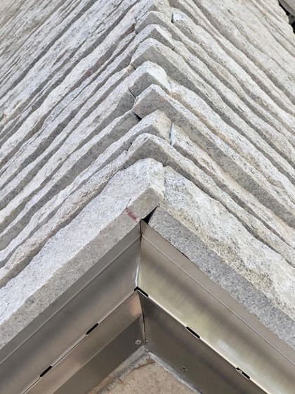 A corner detail of a hand-chiseled stone wall in progress. Stone is a geological material, and we work with it to express its weight, texture, and history, treating it as the skin of the building.