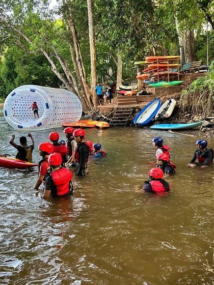 Campers gather by the river at our Dandeli site, with a water roller and kayaks ready for action.