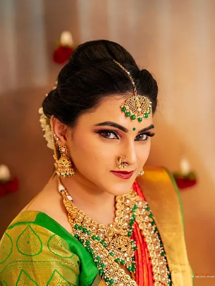 A striking close-up portrait where the model looks directly at the camera. This engaging shot beautifully captures the details of the maang tikka, nose ring, and layered necklaces against the vibrant green blouse.