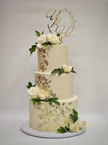 A three-tier wedding cake featuring white and gold leaf details and a custom initial topper.