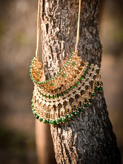 A creative shot of the bride's kundan and green bead necklace hanging on a tree trunk, highlighting its beauty in natural light.