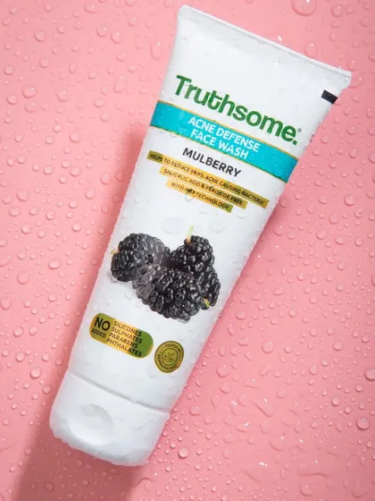 This image for Truthsome's acne defense face wash uses a simple, textured pink background with water droplets to create a clean, clinical, yet appealing look for the skincare product.
