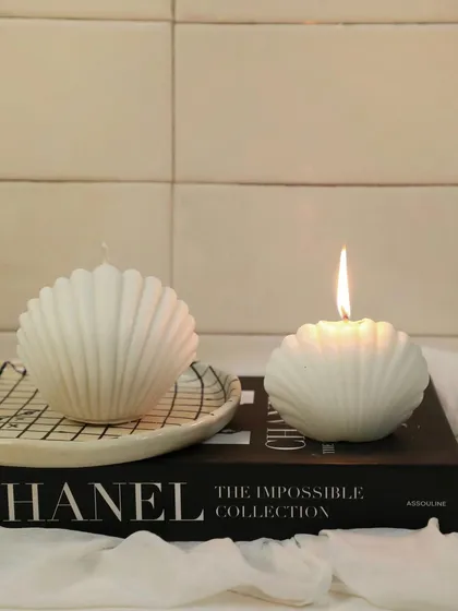 The world is your oyster. Our beautiful shell candles, one lit and one unlit, styled on a stack of books for a chic look.