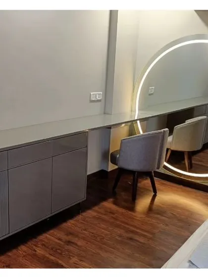A custom-designed dressing table and storage unit in a soft grey finish, paired with a large, backlit circular mirror. This setup creates a functional and glamorous space for daily routines.