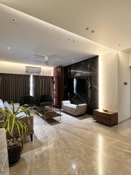 A modern living room where we used a dark marble feature wall for the TV unit to create a dramatic focal point. The surrounding space is kept light and airy with neutral tones and clean lines.