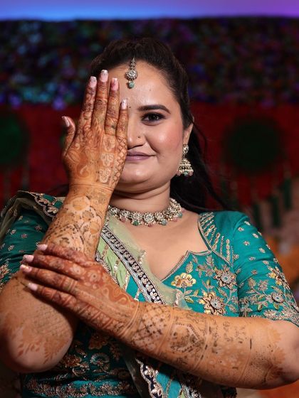 A happy bride posing with her hand over her eye, giving a playful peek at her intricate mehandi.