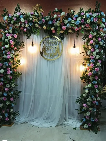 A floral photo booth with a mix of pastel-colored roses and greenery. The custom golden sign in the center can be personalized for any religious or family function.