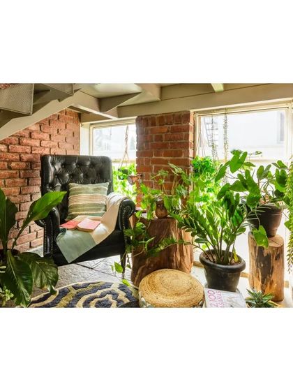A cozy reading corner tucked under the stairs, surrounded by plants. The classic leather armchair and exposed brick wall create a warm, library-like feel.
