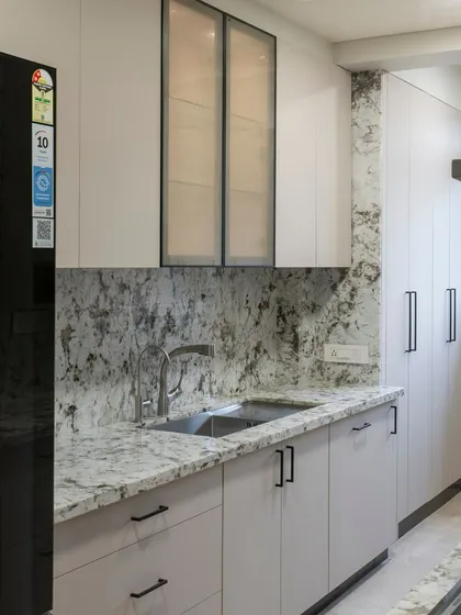 This kitchen uses a striking granite with dramatic veining for both the countertop and backsplash, creating a seamless and impactful look. The light grey cabinets provide a soft, neutral balance.