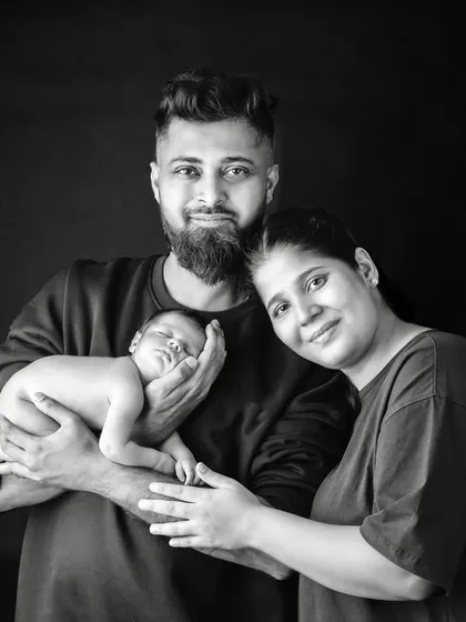A black and white portrait of a new family, with the father proudly holding their sleeping newborn.