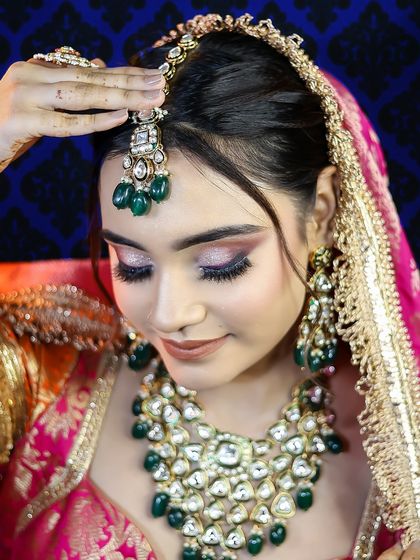 A detailed shot of the bride adjusting her maang tikka, highlighting the jewelry and eye makeup.